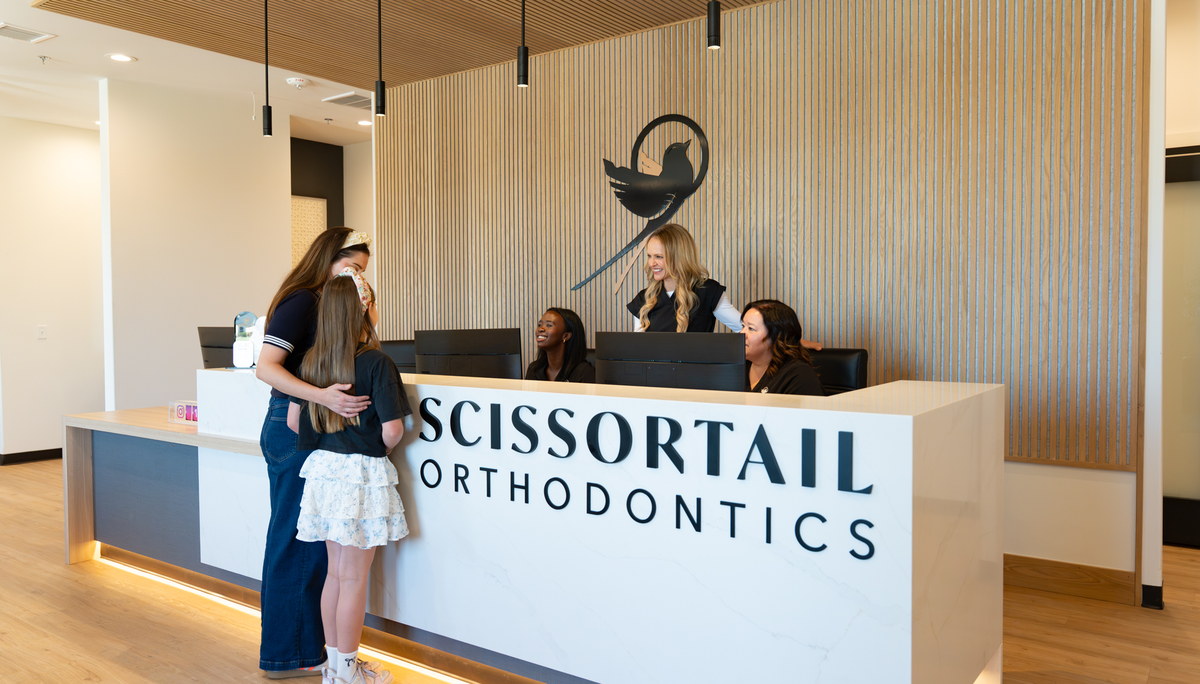 Parent and child checking in with team members at the Scissortail Orthodontics front desk.